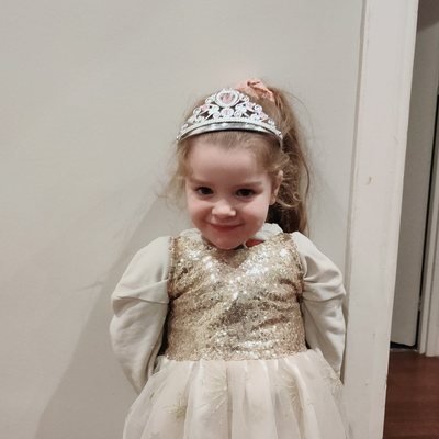 Petite fille déguisée en princesse, diadème et robe à paillettes dorées, tout sourire pendant sa garde Bloom Buddies.