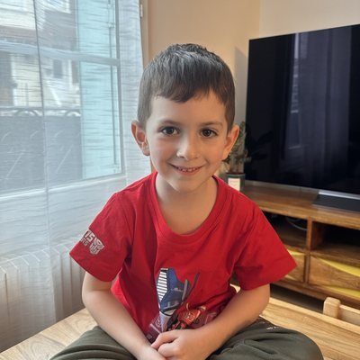 Petit garçon souriant en t-shirt rouge, assis en tailleur dans le salon pendant sa garde.