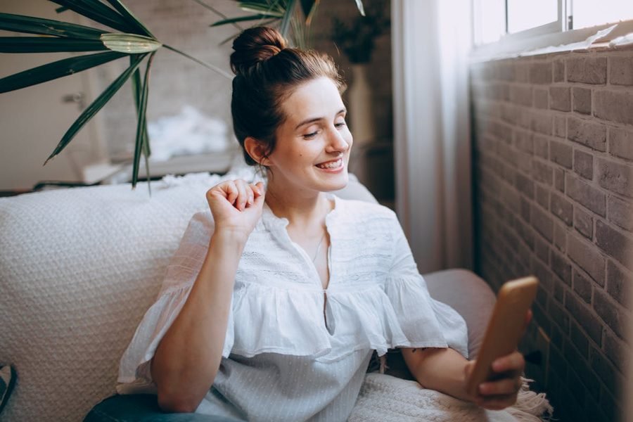 Une maman sourit en découvrant son devis instantané sur son téléphone, installée confortablement chez elle.